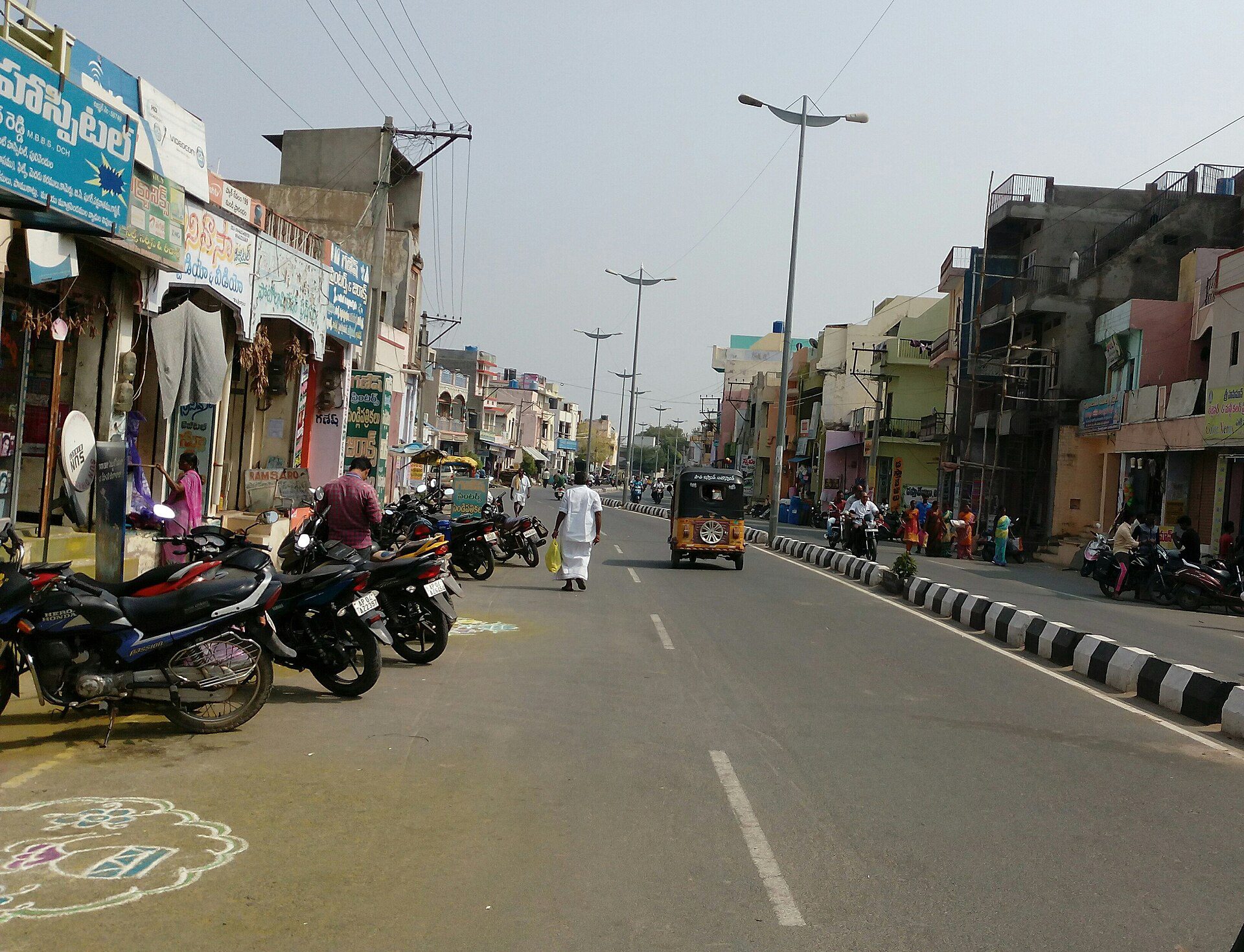 దుకాణాలు, పార్క్ చేసిన ద్విచక్ర వాహనాలు, ఆటోతో పులివెందుల పట్టణంలోని ప్రధాన రహదారి.