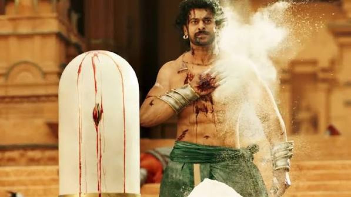 ఎర్రటి చారలున్న ఎత్తైన తెల్లని గుమ్మటం పక్కన, గాయపడిన ఛాతీ, లోహపు కడియాలతో, గాలిలో తెల్లని పొడితో నిలబడిన యోధుడు.