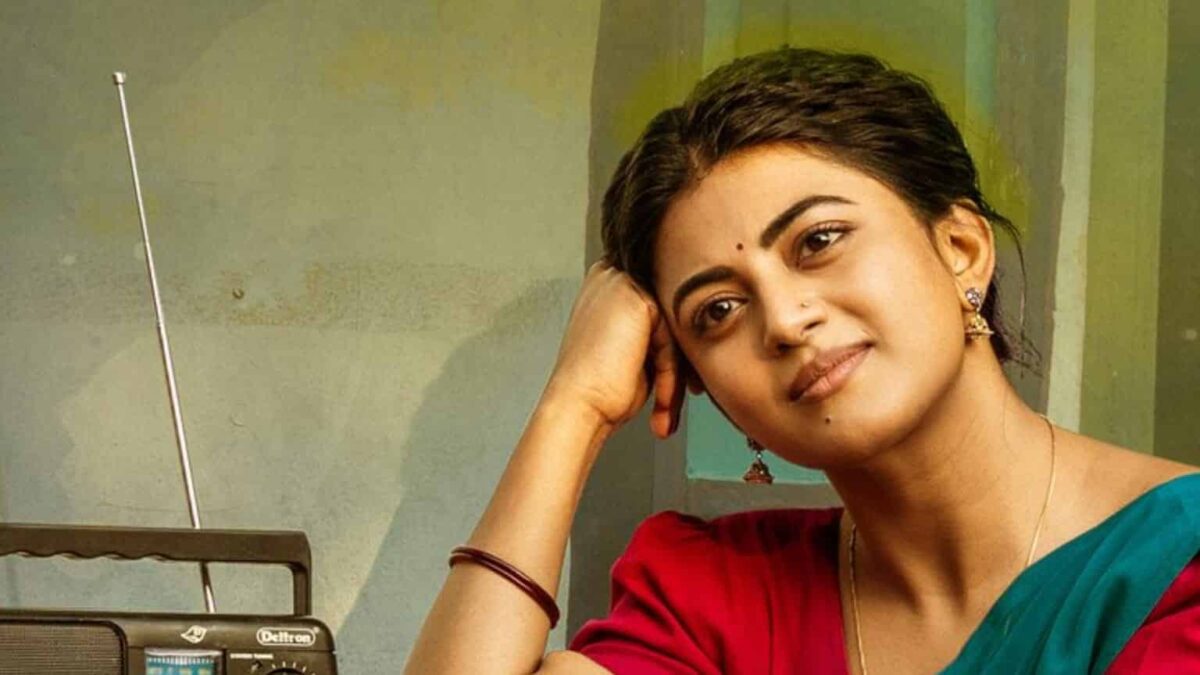 ఎరుపు జాకెట్టు, ఆకుపచ్చ చీరలో పాత రేడియో పక్కన చెంపకు చేయి ఆన్చి నవ్వుతున్న ఆనంది.