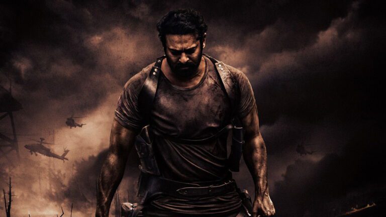 బురదతో తడిసిన చొక్కా, తోలు హోల్‌స్టర్లతో గడ్డంతో ఉన్న ప్రభాస్, వెనుక హెలికాప్టర్లు ఉన్న చీకటి పొగ ఆకాశం కింద నడుస్తున్న దృశ్యం.