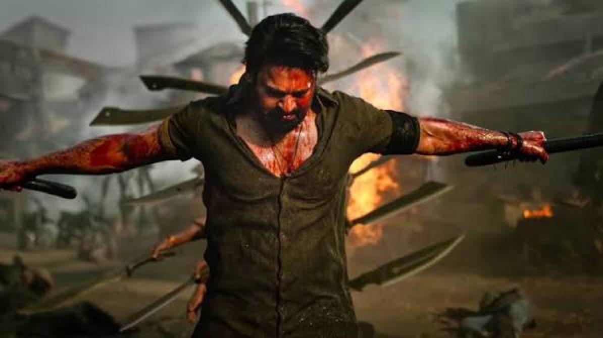 మండుతున్న శిథిలాలు, ఎగురుతున్న కత్తుల మధ్య చేతులు చాచి నిలబడిన, రక్తంతో తడిసిన చిరిగిన నల్ల చొక్కా వ్యక్తి.