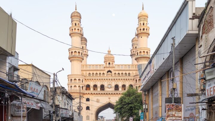 దుకాణాలు, విద్యుత్ తీగలతో నిండిన వీధి చివర కనిపిస్తున్న చార్మినార్.